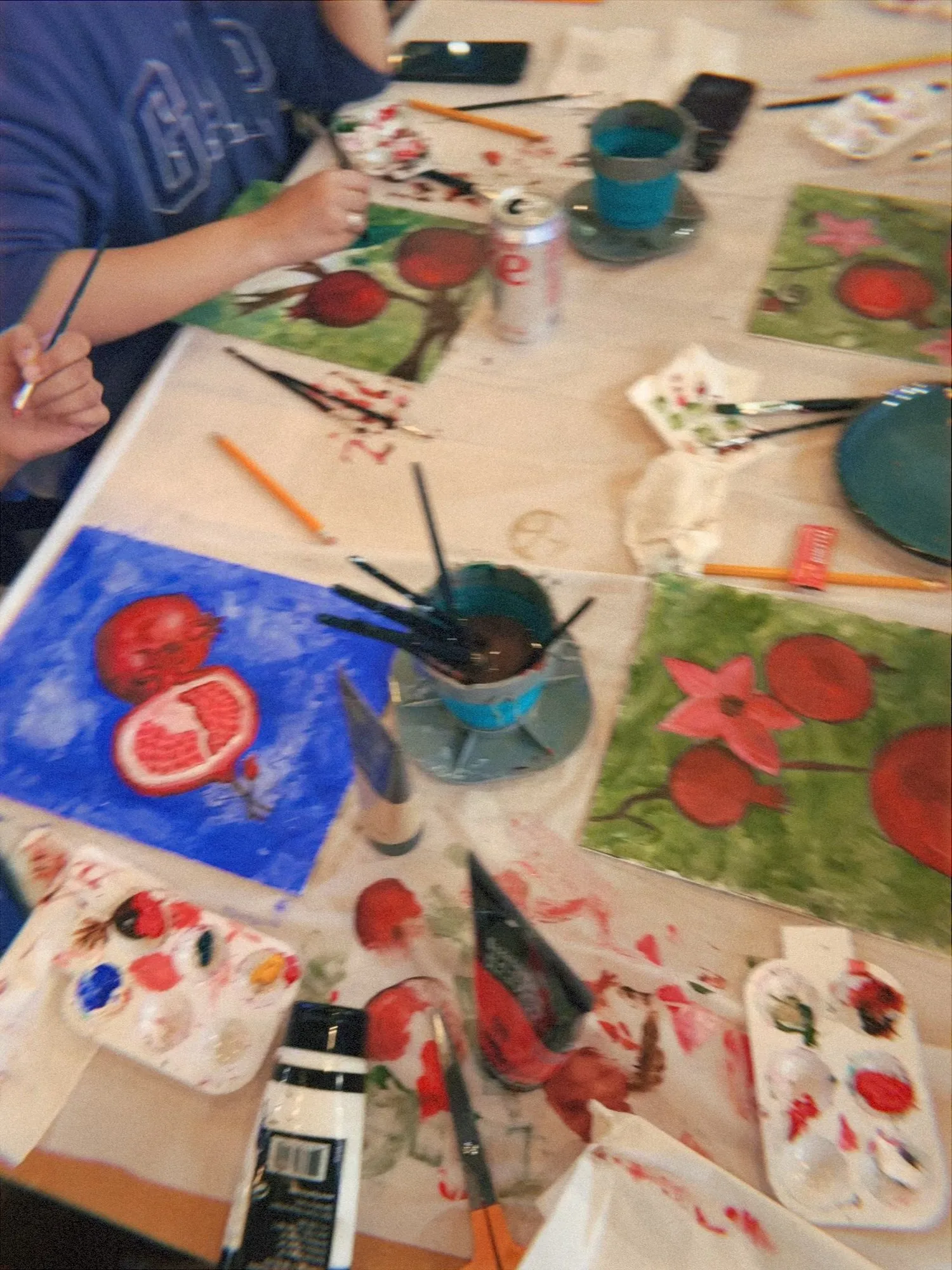 A table covered in pomegranate paintings, brushes, and water cups mid-session.
