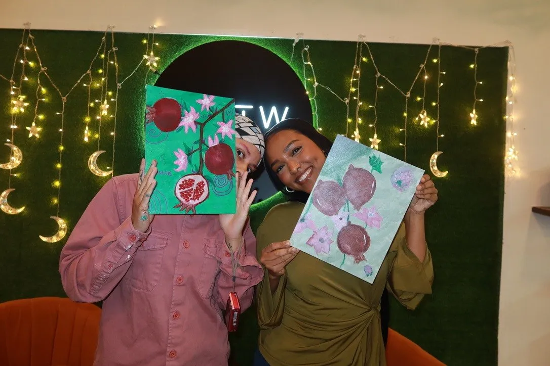 Two guests holding their canvases up in front of their faces, laughing.