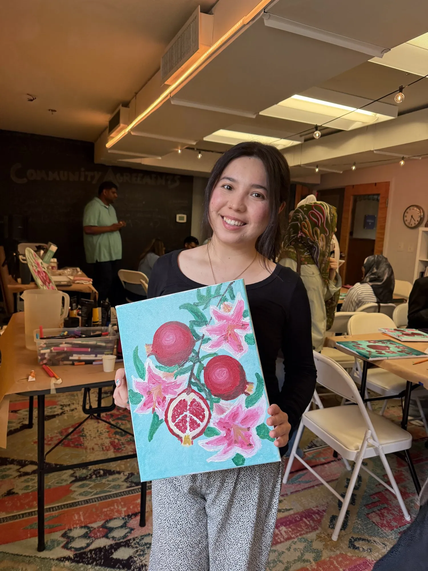 A smiling guest holding her finished pomegranate painting.
