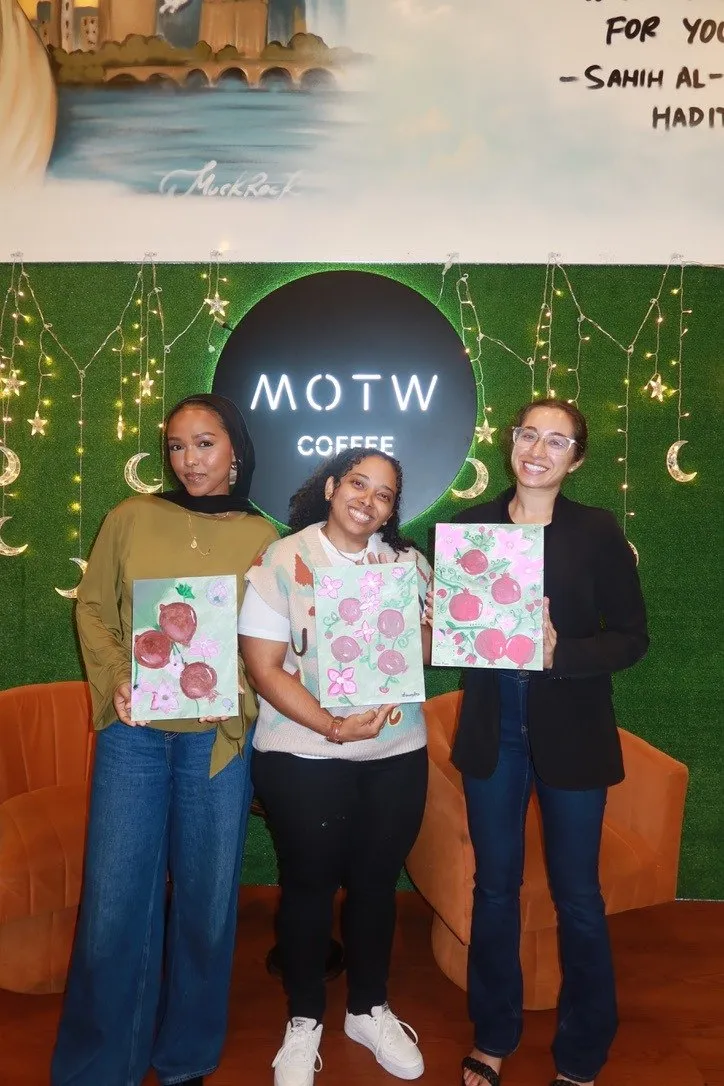Three guests holding their paintings in front of a green leafy wall.