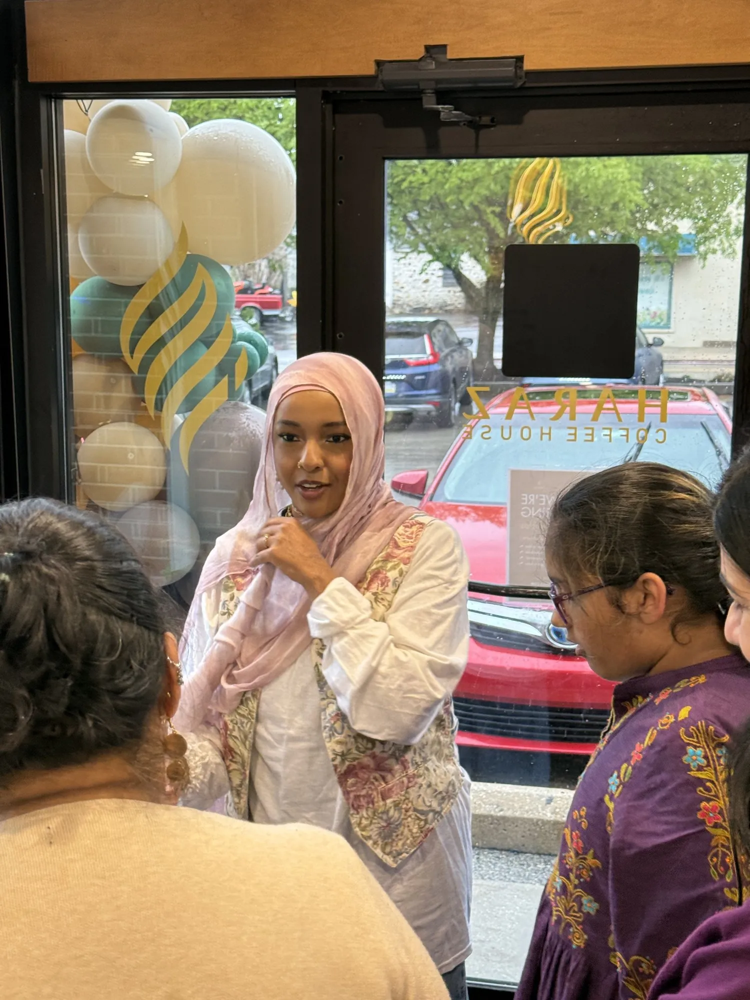 Hanan, in a pink headscarf, speaking to a small group inside a coffee house.