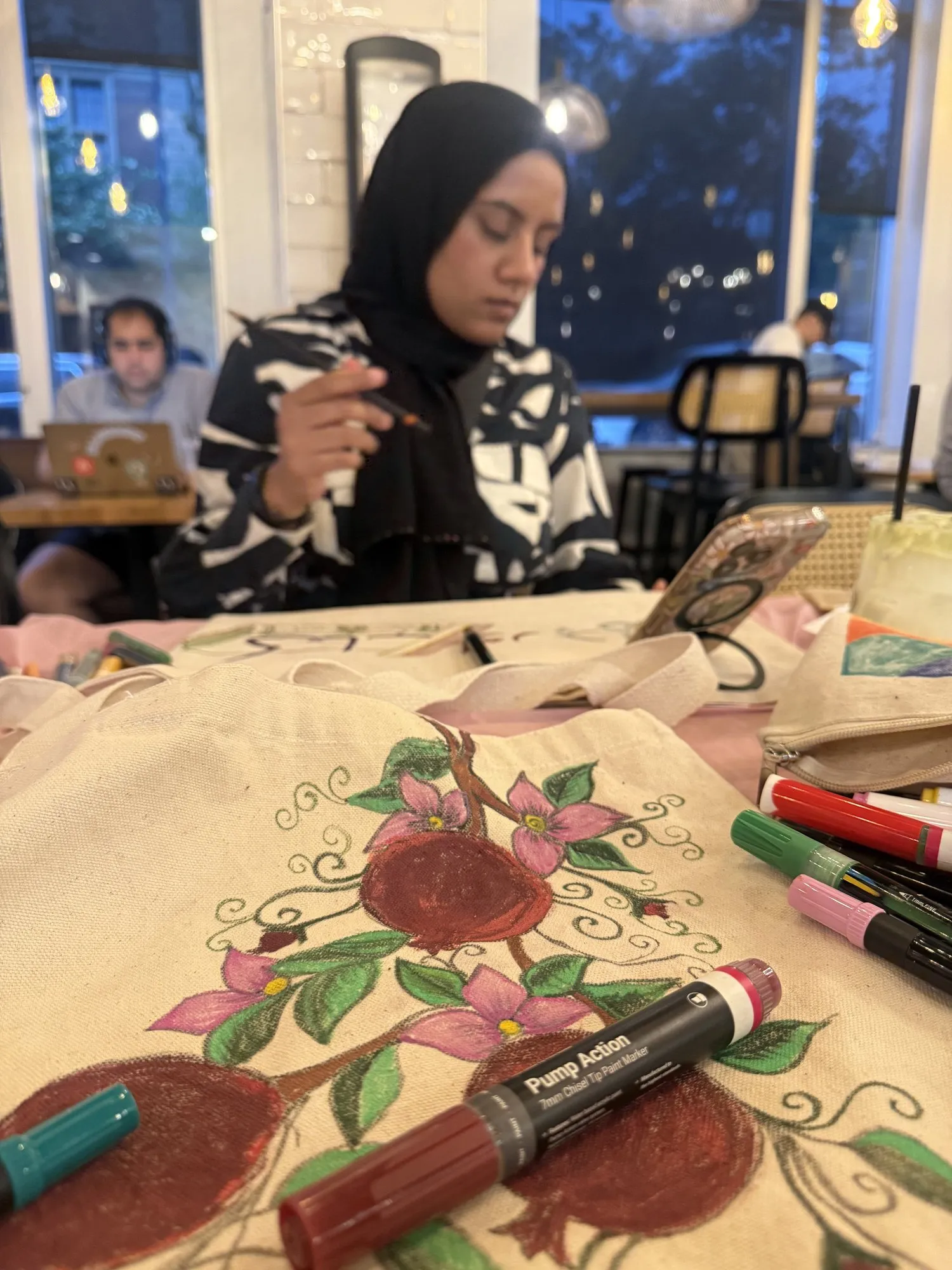 A guest outlining a floral design on a canvas tote bag with paint markers.