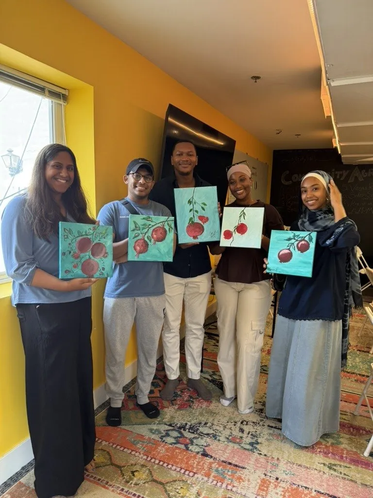 A group posing with their canvases against a yellow wall.