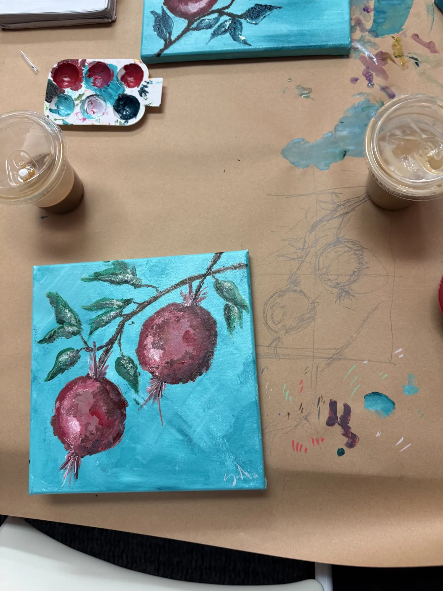 A pomegranate branch painted on a turquoise canvas, seen from above.