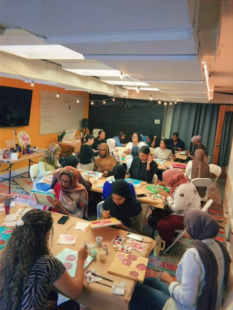 A full room of guests painting at long tables during an evening session.