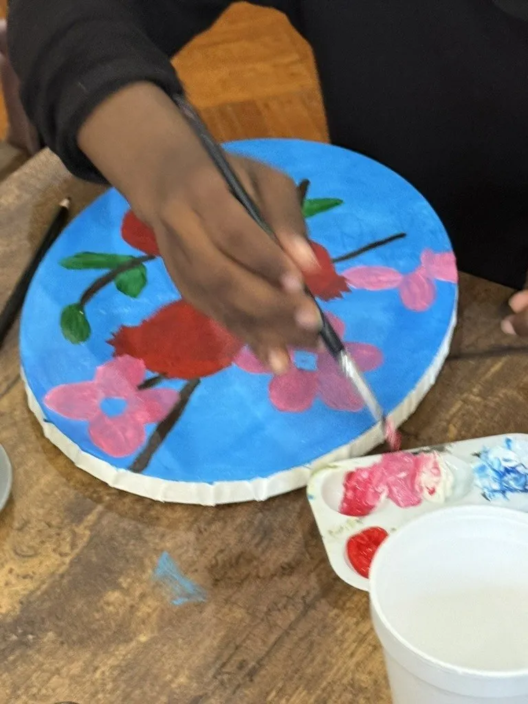 A brush adding red to a round canvas painted sky blue.